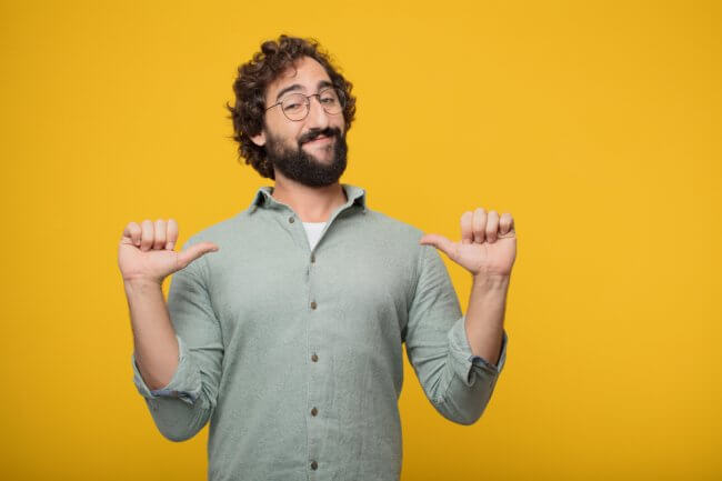 Man with glasses pointing thumbs at chest