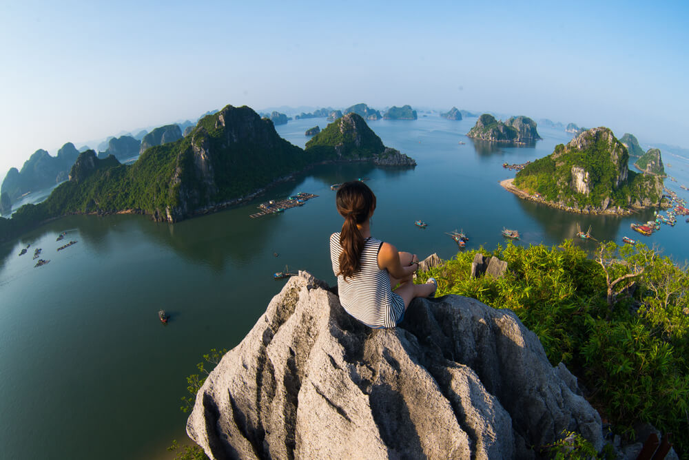 A solo female traveller sitting on top of a mountain in Ha Long Bay