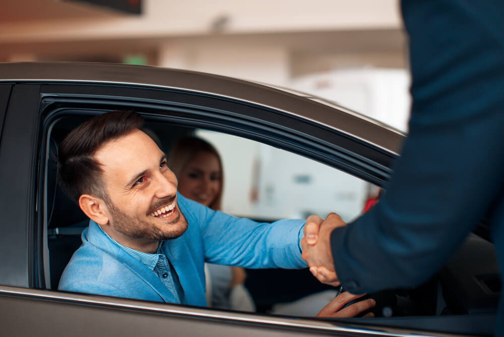 A man sitting in a car shakes someone’s hand