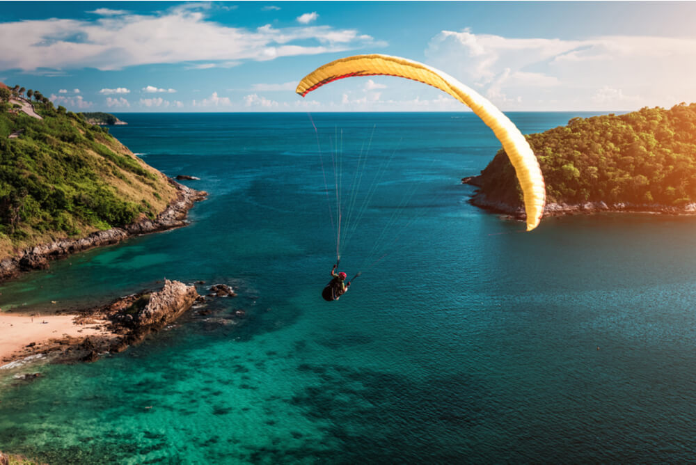 skydiver flying over water at sunset