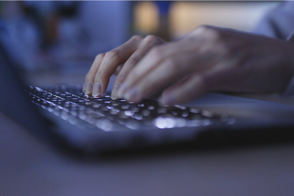 unidentified person typing on a laptop in a dark room