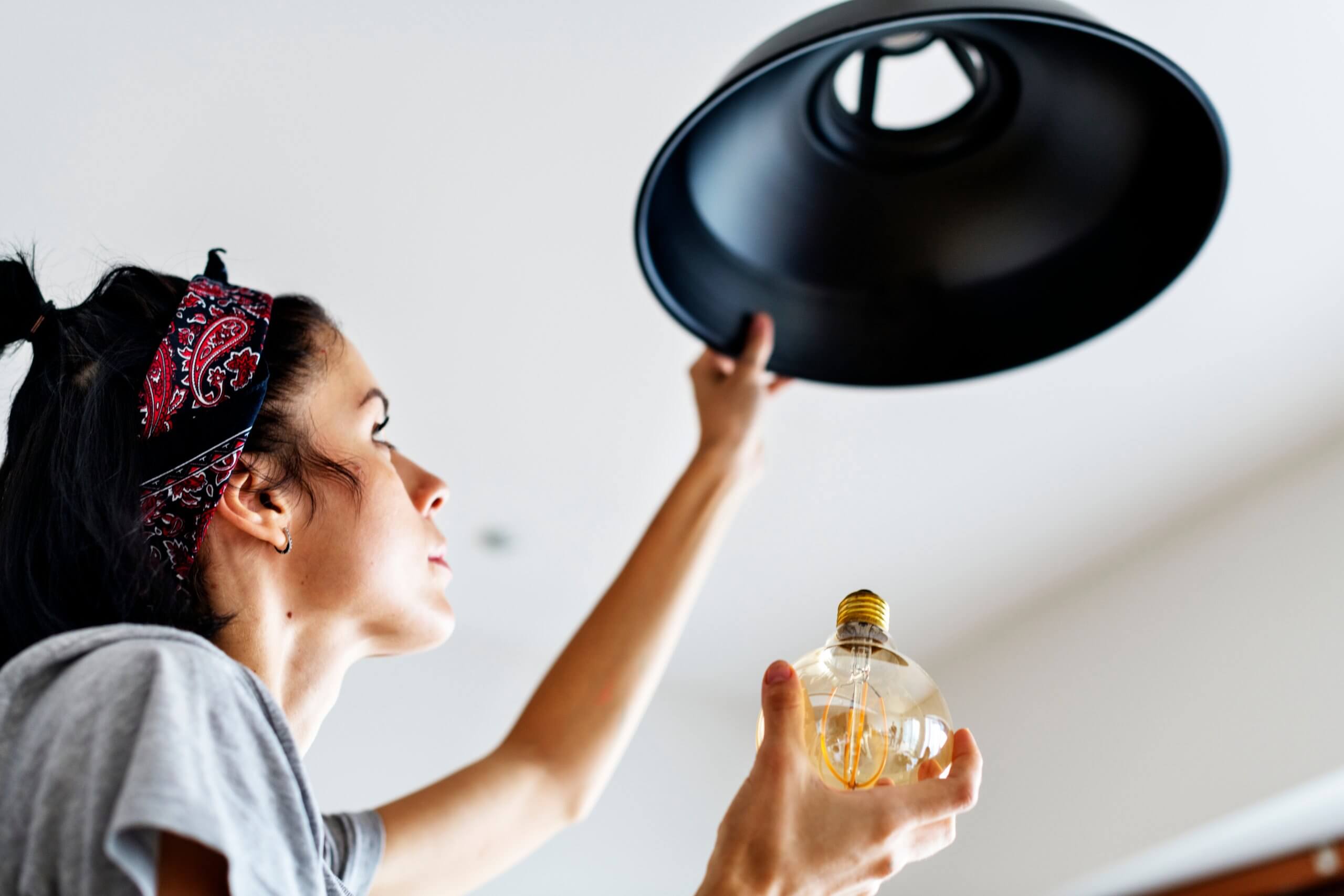 a woman changing a lightbulb in a black pendant light