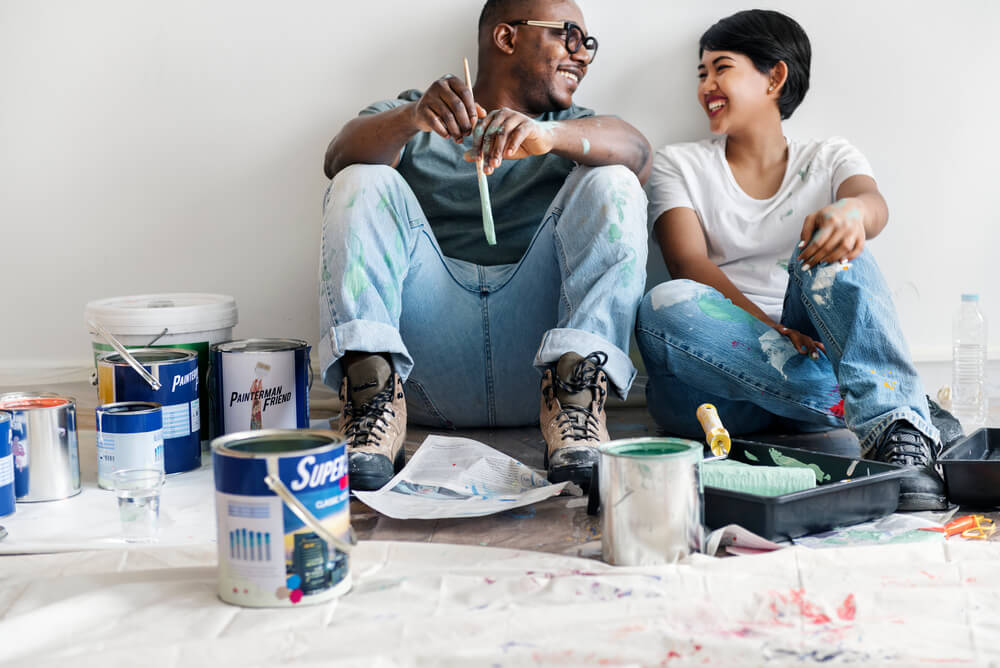 a man and woman sitting down among painting equipment