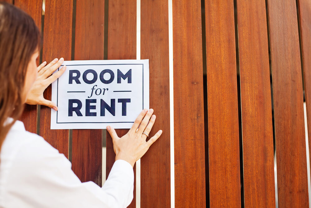 a woman putting up a room for rent sign
