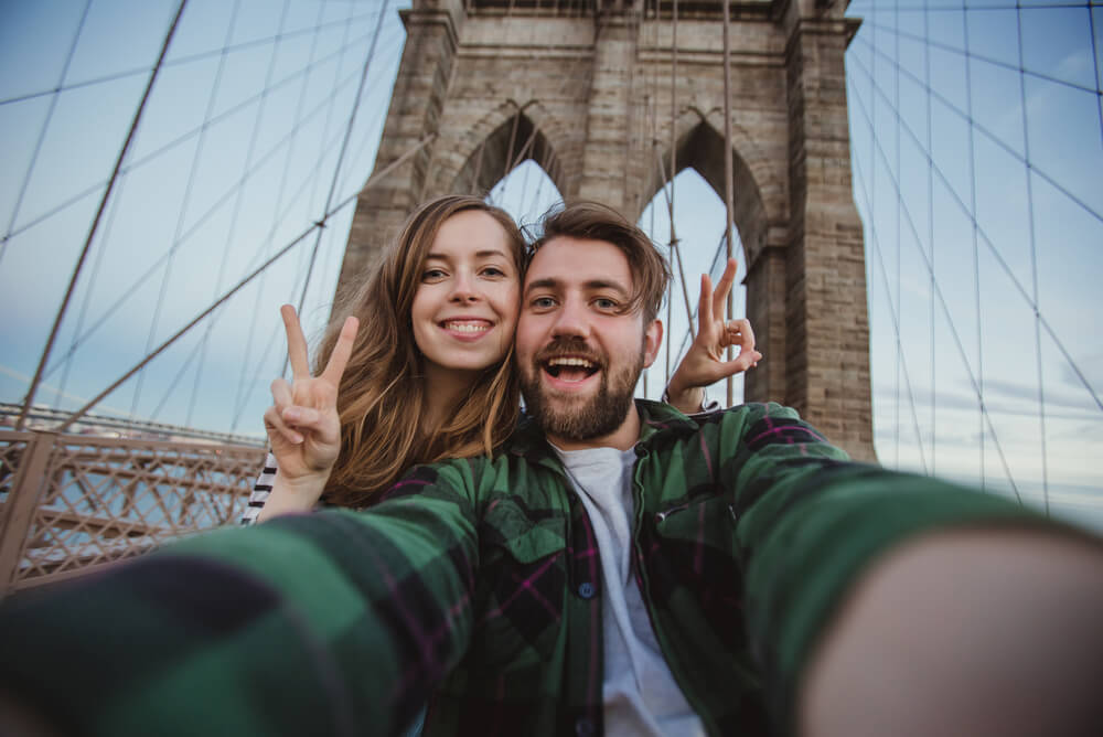 Couple with personal liability insurance taking selfie on Brooklyn bridge