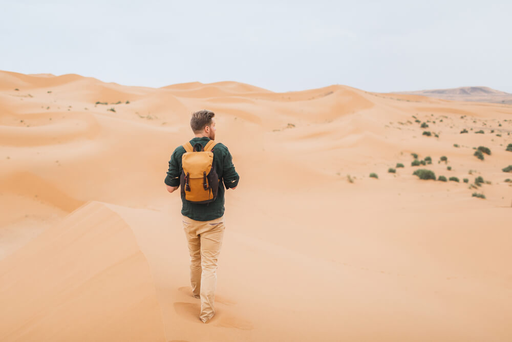 a man walking through the sand dunes of the Sahara