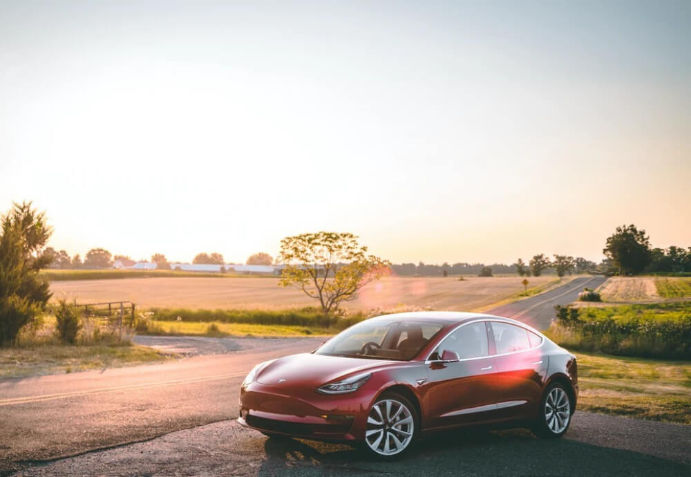 a red Tesla Model 3 parked to the side of the road in rural Australia