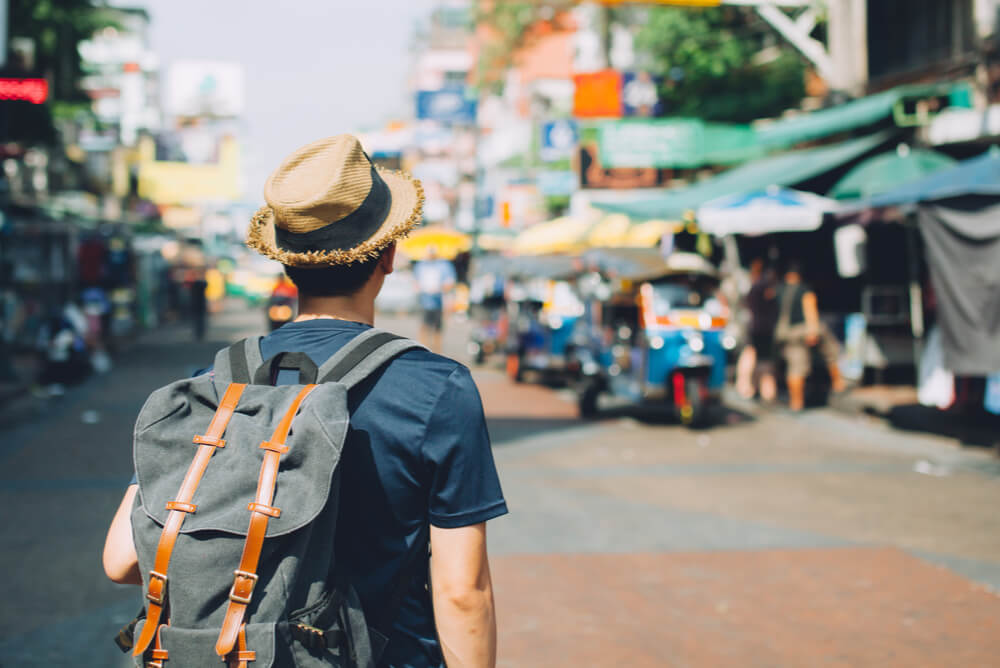 man with backpack walks through a market in Thailand