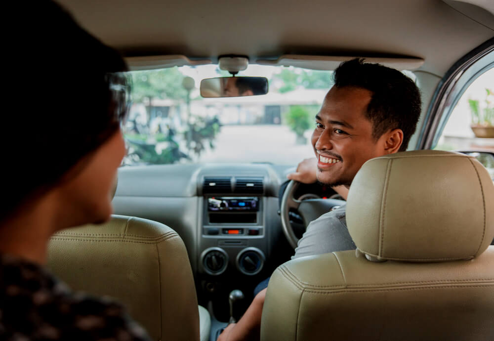 a rideshare driver looks at passenger in backseat and smiles