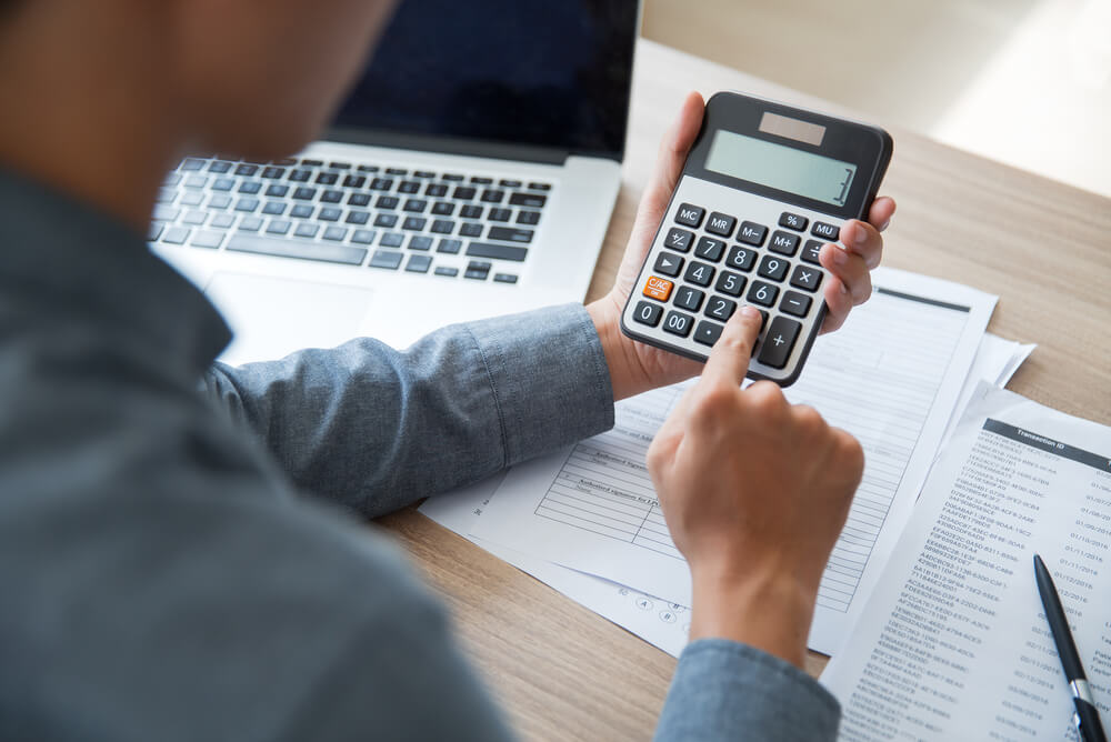 Man using a calculator with paperwork and a laptop